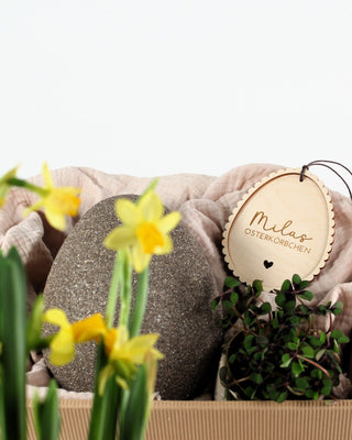 Osterkörbchen mit personalisiertem Osteranhänger und Narzissen im Vordergrund.
