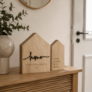 Personalisiertes Deko-Haus aus Holz mit Schriftzug „Home“ und gravierten Koordinaten auf stilvollem Holz Sideboard.