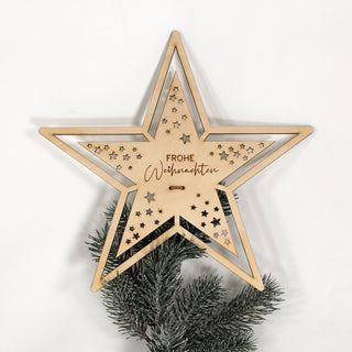 Filigrane Weihnachtsbaumspitze aus Holz in Sternform mit ausgestanzten Sternen und der Aufschrift „Frohe Weihnachten“.