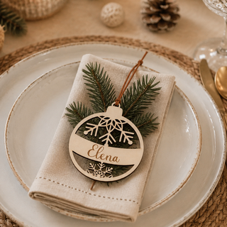 Personalisierte Weihnachtskugel aus Holz mit Schneeflockenmotiv und eingraviertem Namen als Tischdekoration auf einer liebevoll gedeckten Weihnachtstafel.