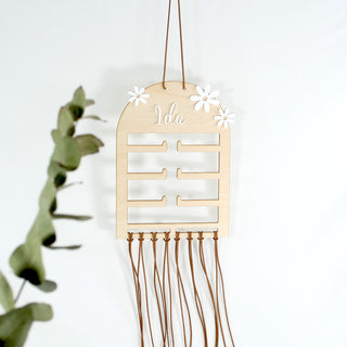 Personalisierter Haarspangenhalter aus Holz mit Namen „Ida“, mehreren Steckplätzen für Haargummis und langen Bändern zur Aufbewahrung von Haarspangen und Clips, dekoriert mit Blumen-Elementen.
