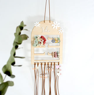 Personalisierter Haarspangenhalter aus Holz mit Namen „Ida“, mehreren Steckplätzen für Haargummis und langen Bändern zur Aufbewahrung von Haarspangen und Clips, dekoriert mit Blumen-Elementen. Haargummis und Haarklammern abgebracht