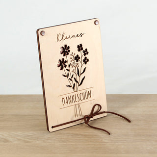 Nahaufnahme des filigranen Blumenstrauß-Laserschnitts auf der Holz-Geschenkkarte, durch den der Geldschein hindurchscheint