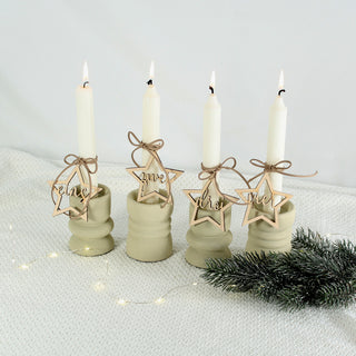 Set aus vier gelaserten Holzanhängern in Sternform mit den Aufschriften eins, zwei, drei und vier – dekoriert an weißen Adventskerzen auf neutralem Hintergrund.