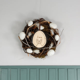 Personalisierter Osteranhänger aus Holz mit Hasenohren im Ei, gelasert mit Namen. Osterlich dekoriert in einem Kranz.