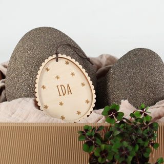 Personalisierter Osteranhänger aus Holz in Osterei-Form mit Blumenmuster und Namen. Dekoriert in einem Oster Nest.
