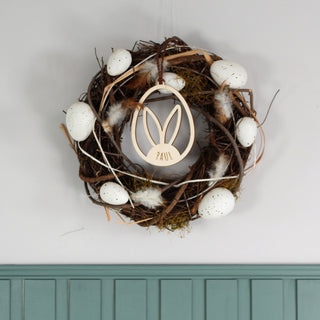 Personalisierter Osteranhänger aus Holz mit Hasenohren im Ei, gelasert mit Namen. Moderne Osterdekoration zum Aufhängen, dekoriert an einem Oster Kranz.