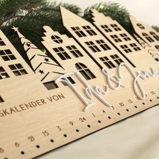 Detailansicht Gravur und Schriftzüge personalisierter Adventskalender aus hellem Holz mit filigranem Häuser-Motiv.