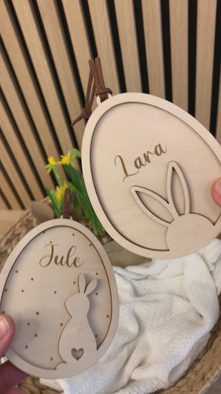 Video von personalisierten Osteranhängern aus Holz mit Hasenohren im Ei, graviert mit Namen. Vor Osterkorb mit Narzissen